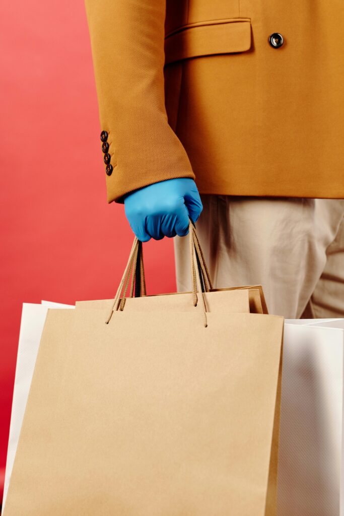 A fashionable photo of a gloved hand holding shopping bags with a red backdrop.